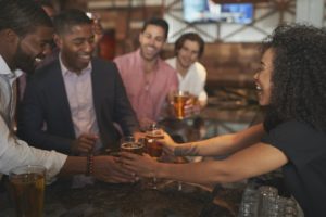 Barmaid Serving Group Of Male Friends On Night Out For Bachelor Party Making Toast Together